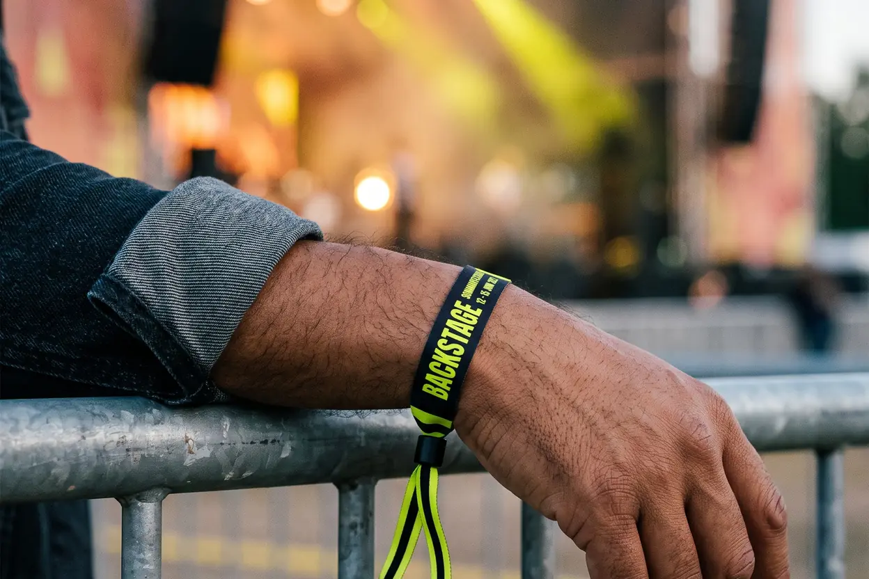 Arm på kravallstaketet framför en festivalscen med ett svart och gult tygband, BACKSTAGE
