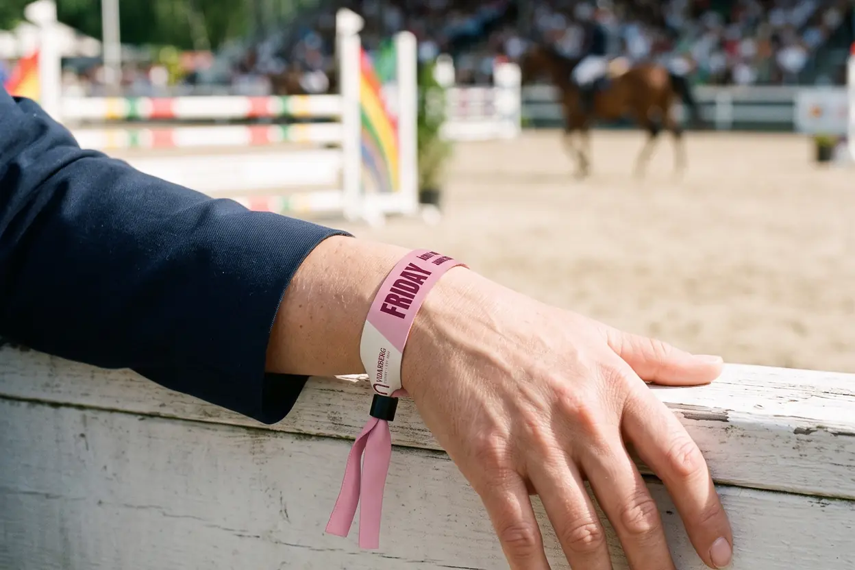 Hand på staketet vid en hopptävling med ett rosa tygband, FRIDAY, och en sponsorlogga i ett ljust fält