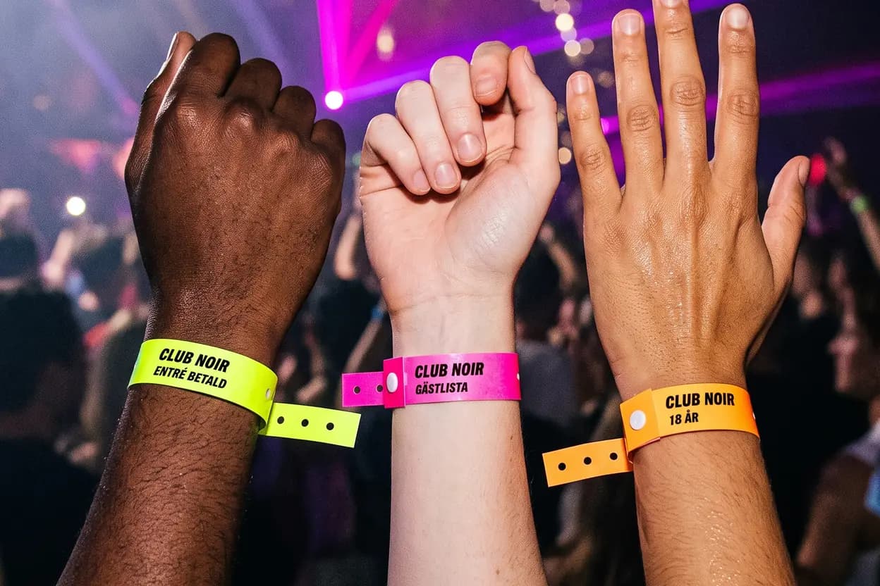 Tre uppsträckta händer på ett dansgolv med vinylband i neongult, neonrosa och orange: ENTRÉ BETALD, GÄSTLISTA och 18 ÅR