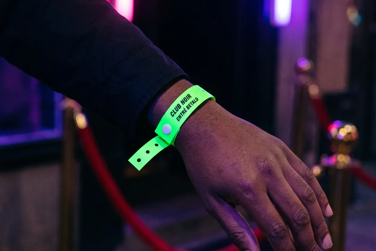 Hand vid en klubbentré med ett neongrönt vinylband, CLUB NOIR ENTRÉ BETALD